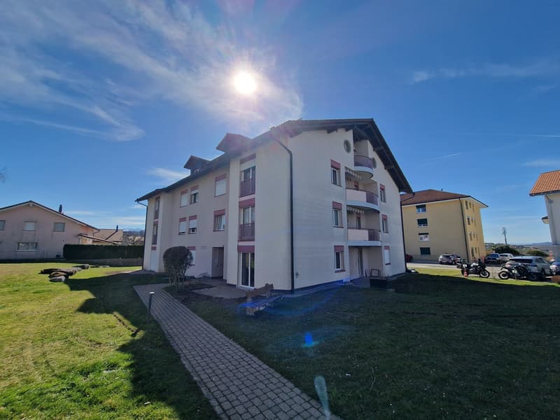 3 story apartment building, white exterior, red trim, balconies, brick walkway, grassy area, parked cars