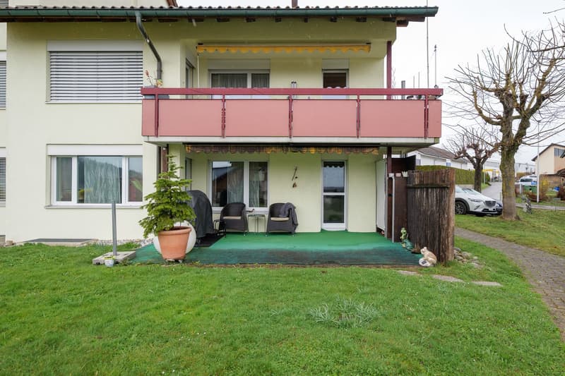 2 story house, beige exterior, red balcony railing, 2 chairs, potted plant, green flooring