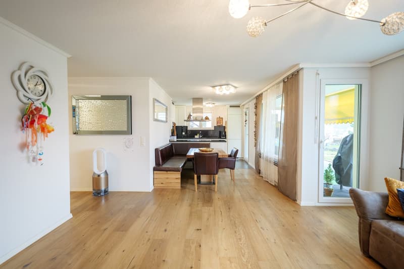 Living room, hardwood floors, dining area, modern lighting, beige sofa, dining table with chairs, window with curtain, wall clock, mirror, air purifier, potted plants