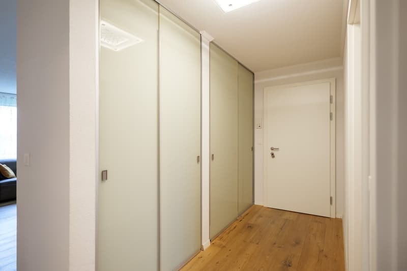 empty room, three glass sliding doors, wooden floor, white walls, entrance door, light ceiling
