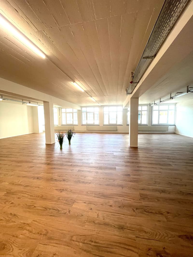 large room, wooden floor, high ceiling, white walls, multiple windows, two flower vases