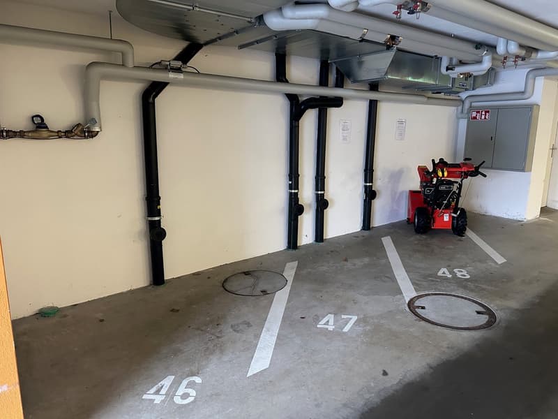 Underground parking garage with floor numbered parking spaces and pipes along the walls.