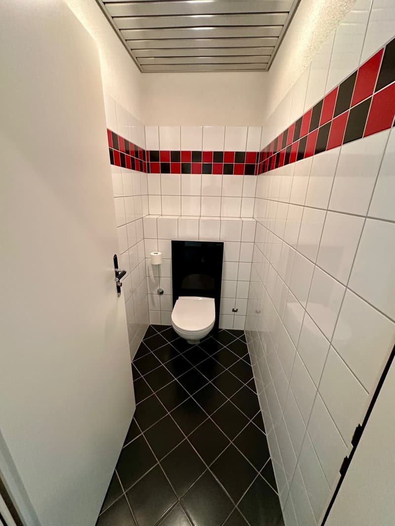 Small bathroom with white and red tiles, black floor, white toilet, white door