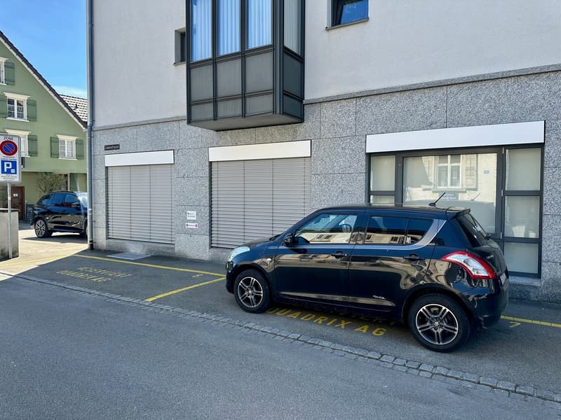 Building with two garages, a car parked in front, and a no parking sign