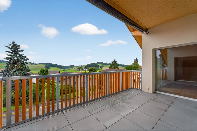 A balcony with wooden railings, tiled floor, and a view of a green landscape