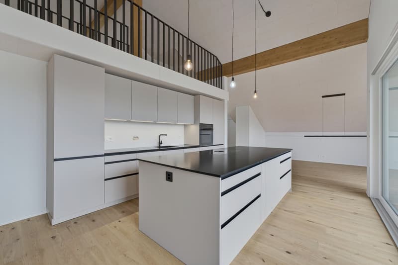 Modern kitchen with white cabinets, black countertop, central island, wooden floor, and modern lighting.