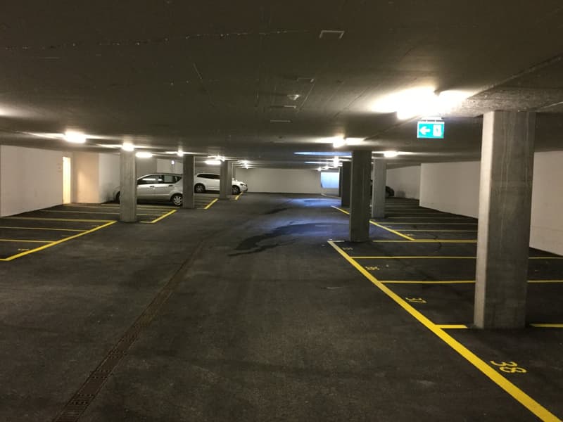 underground parking area, gray concrete walls, yellow markings, 3 cars parked