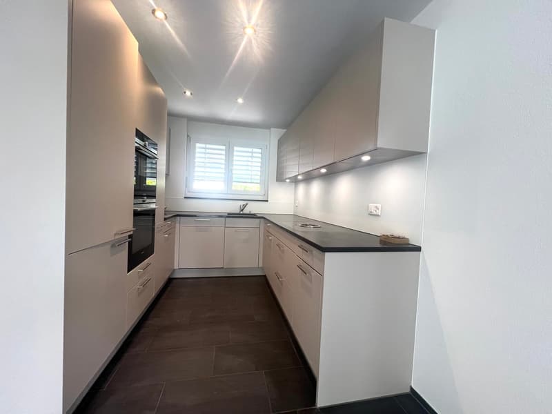modern kitchen with white cabinets, black countertops, built-in oven and dishwasher, sink with faucet, window with blinds
