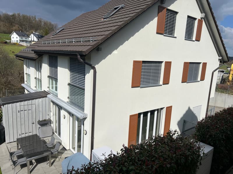 2 story house, white exterior, brown roof, brown shutters, large windows, patio with table and chairs