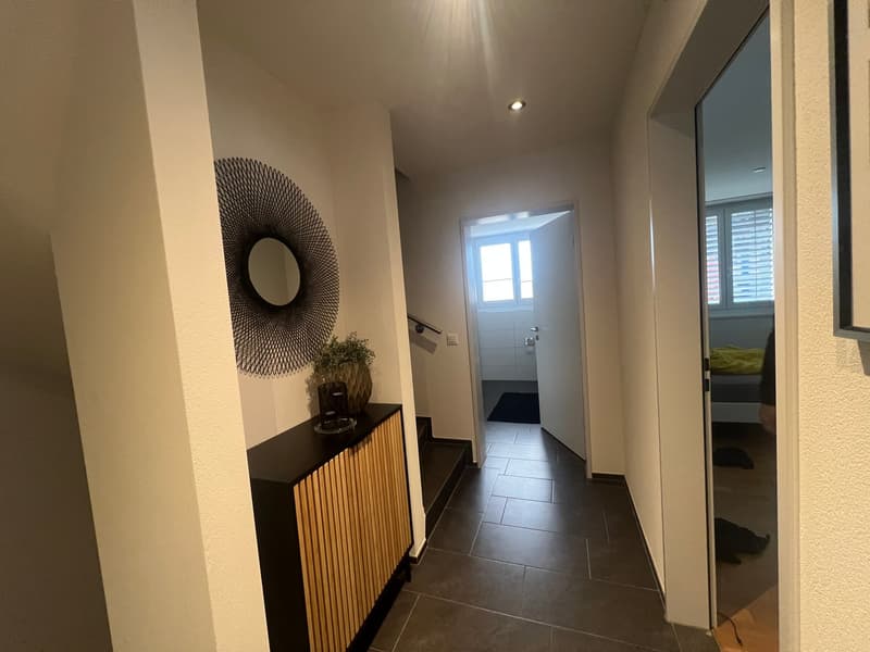 hallway with white walls, black tiled floor, wooden cabinet with a plant, mirror, open door leading to a room with a bed