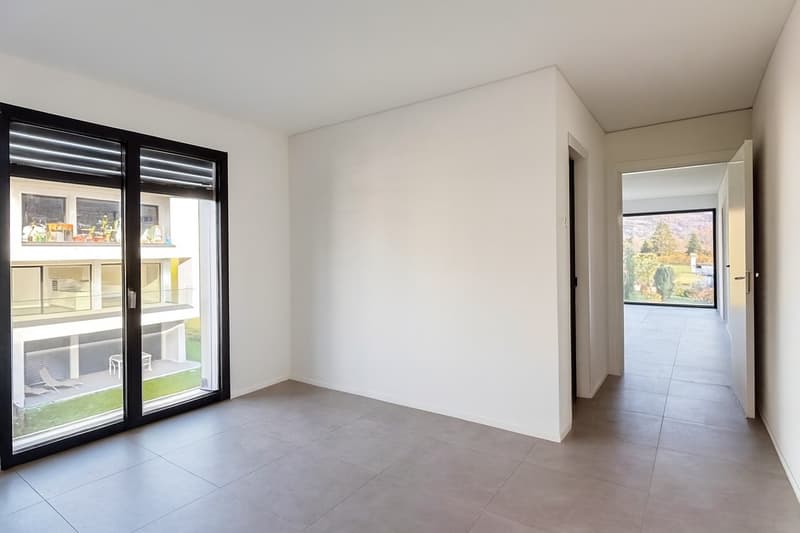 Empty room with gray floor, large windows, open doors, balcony with garden view