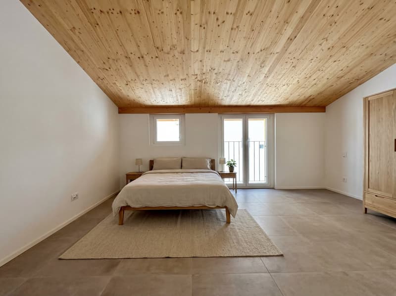 Bedroom: a wooden bed with white linens, two nightstands with lamps, white walls, wooden ceiling, tiled floor, a carpet, two windows, and a glass door leading to a balcony.