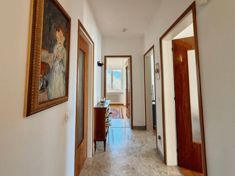 long hallway, white walls, wooden doors, marble floor, picture frame, wooden cabinet, radiator, rug, window
