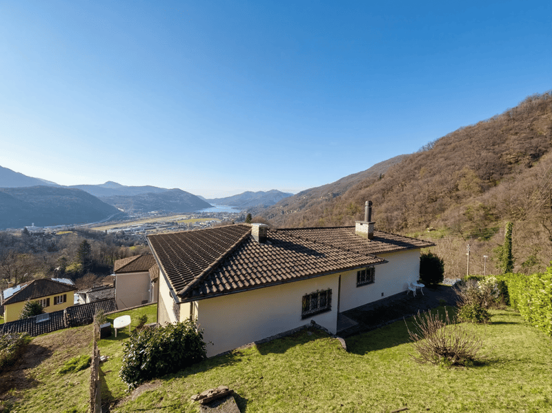 Detached house, brown roof, white walls, two chimneys, surrounded by greenery, mountain view