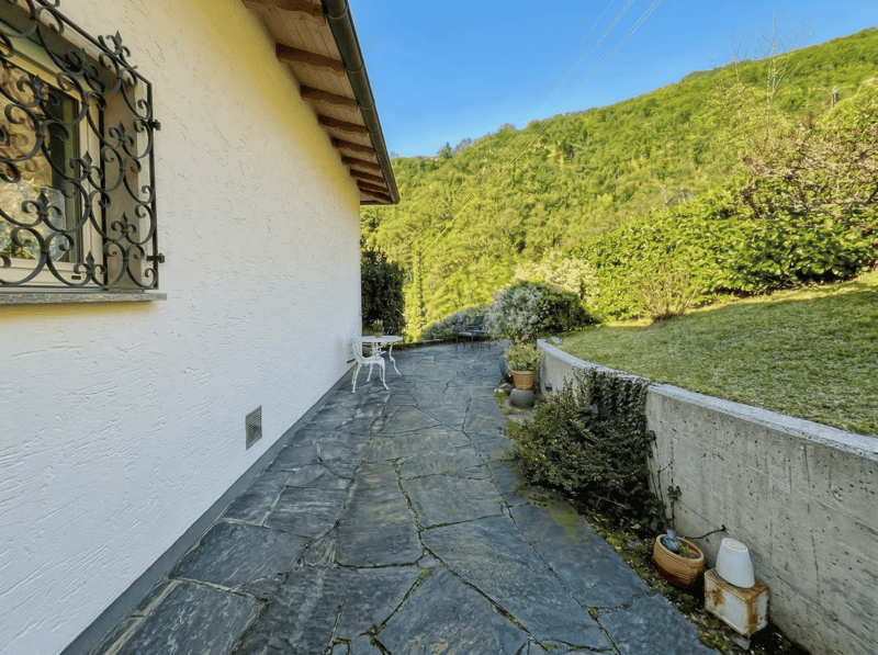 Stone pathway, white wall, table and chairs, plants, green hillside