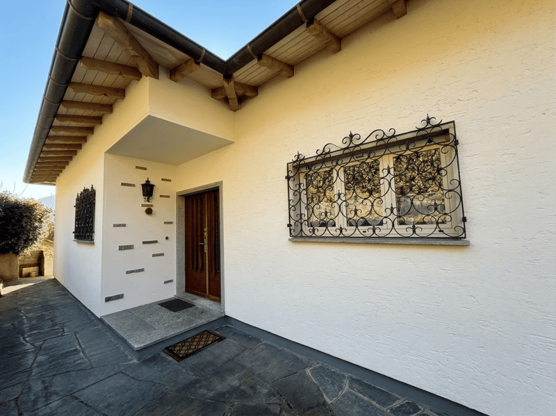 white exterior, wooden door, black metal window grill, black roof, stone pathway