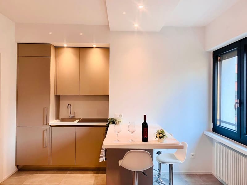 modern kitchen with white countertops, wooden cabinets, white chairs, wine bottle, wine glasses, flowers, radiator, window
