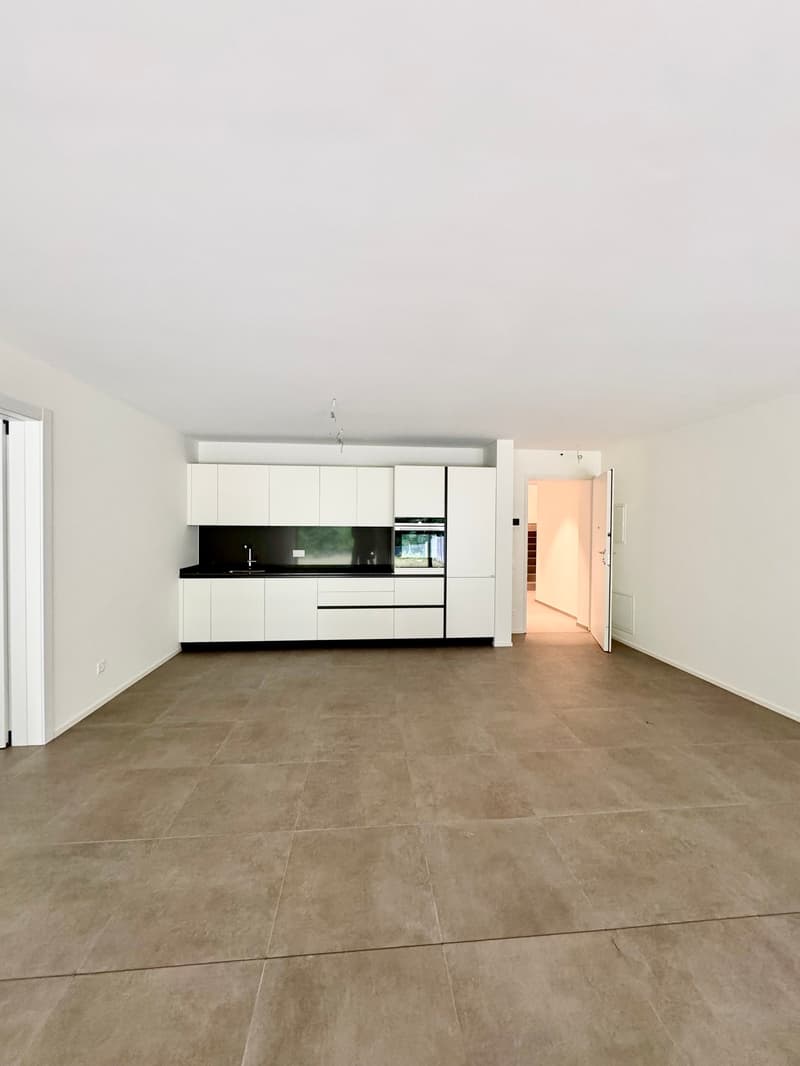 Empty room with white walls, tiled floor, white kitchen cabinets, black countertop, open door
