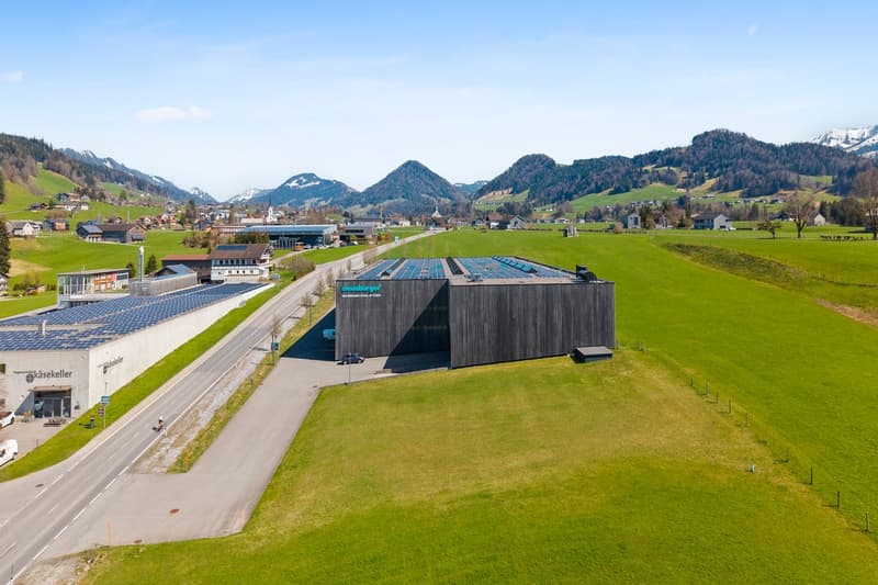 Industrial building with solar panels, situated in a rural landscape with mountains in the background