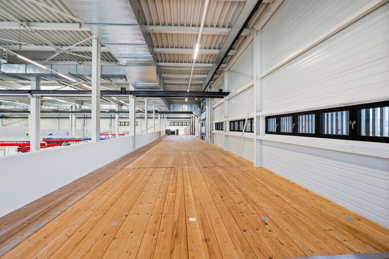 Large hall with long corridor, wooden floor, white walls, windows with black frames, beams on ceiling