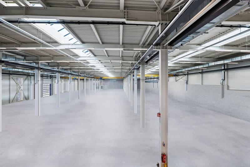 Empty warehouse with high ceilings, metal beams, exposed lighting, white flooring, fire extinguisher