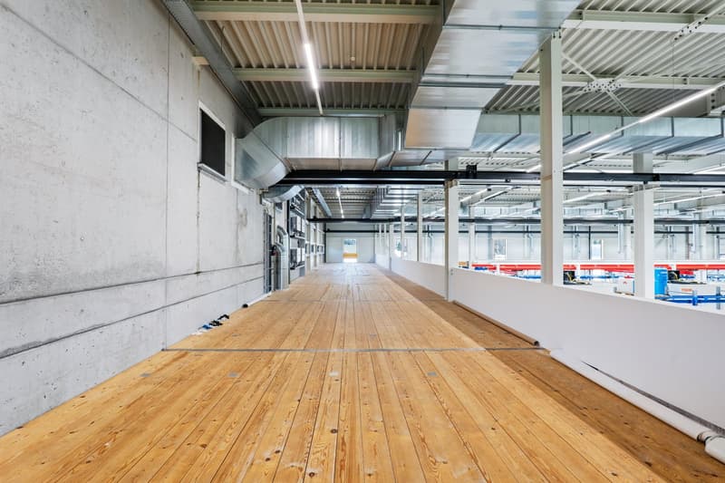 wide corridor with wooden flooring, concrete wall, exposed beams, steel beams, lights