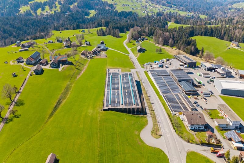 Industrial complex with multiple buildings, one prominently featuring large solar panels on its exterior.