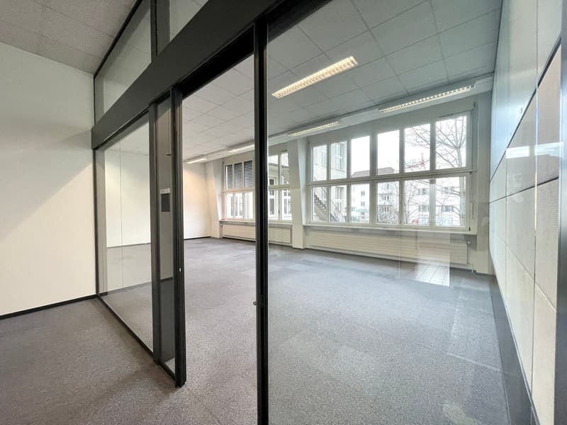 Empty room with large windows, glass doors, grey carpet floor, suspended ceiling with lights, white walls
