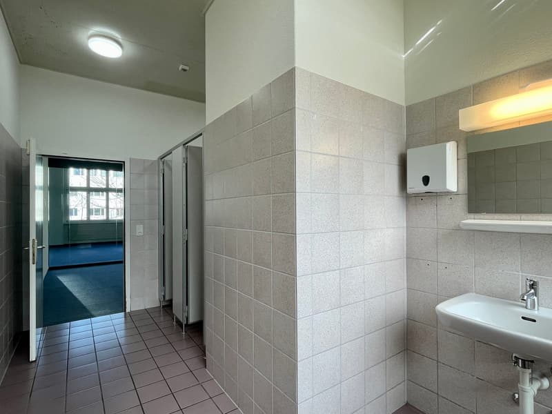 Empty bathroom, white tiled walls, floor, sink, faucet, mirror, and a wall-mounted soap dispenser.