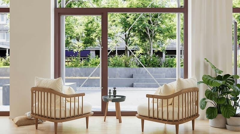 A room with a glass door opening to a garden view, featuring wooden lounge chairs with pillows, a small table, and a potted plant