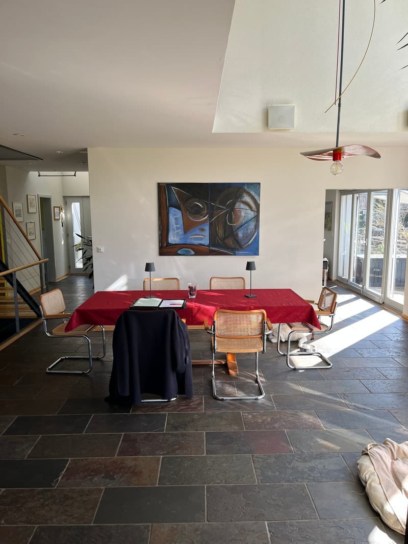 Dining table, red tablecloth, 6 chairs, lamps, painting, black floor, white walls, windows
