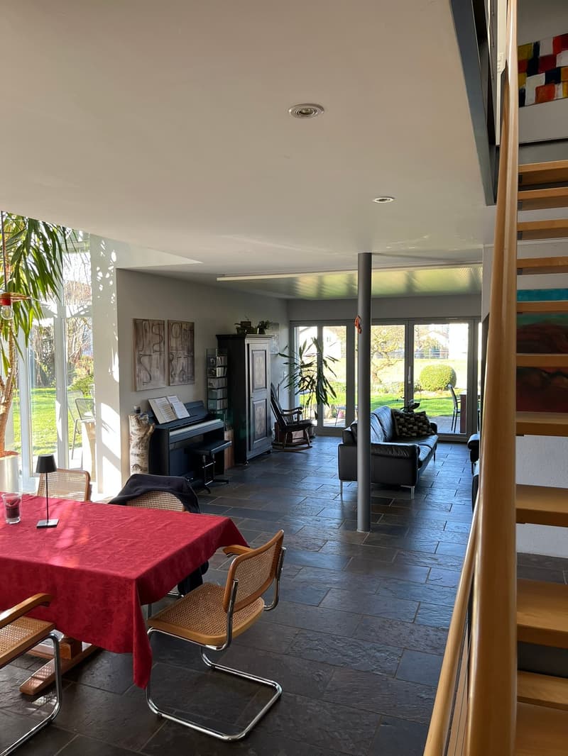 large open space, red dining table, wooden chairs, piano, leather sofa, large windows