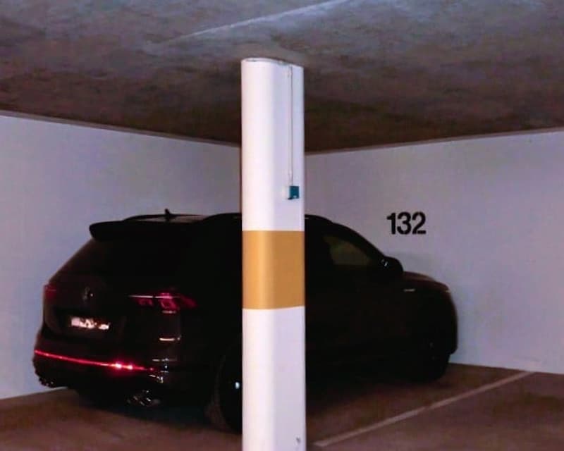 Parking space with a car parked, white and yellow column, number 132 on the wall