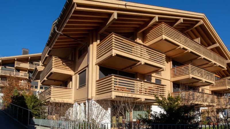 Modern wooden apartment building with multiple balconies, large windows, and a sloped roof