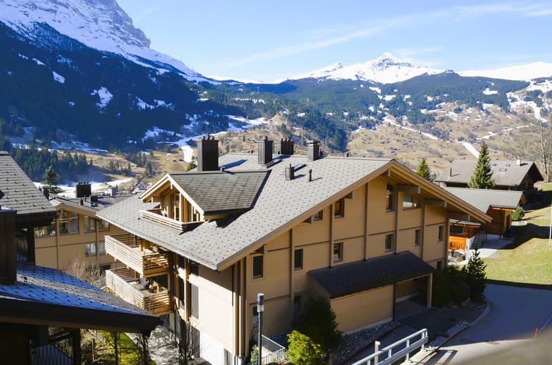 Mountainside chalet with multiple balconies, gray roof, surrounded by snow-capped mountains