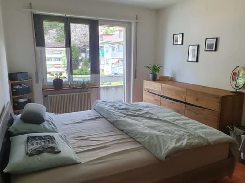 large double bed, wooden chest of drawers, window, balcony, plants, radiator, nightstand with shelves