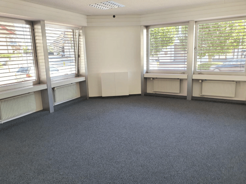 Empty room with three windows, grey carpet, radiators, ceiling lights