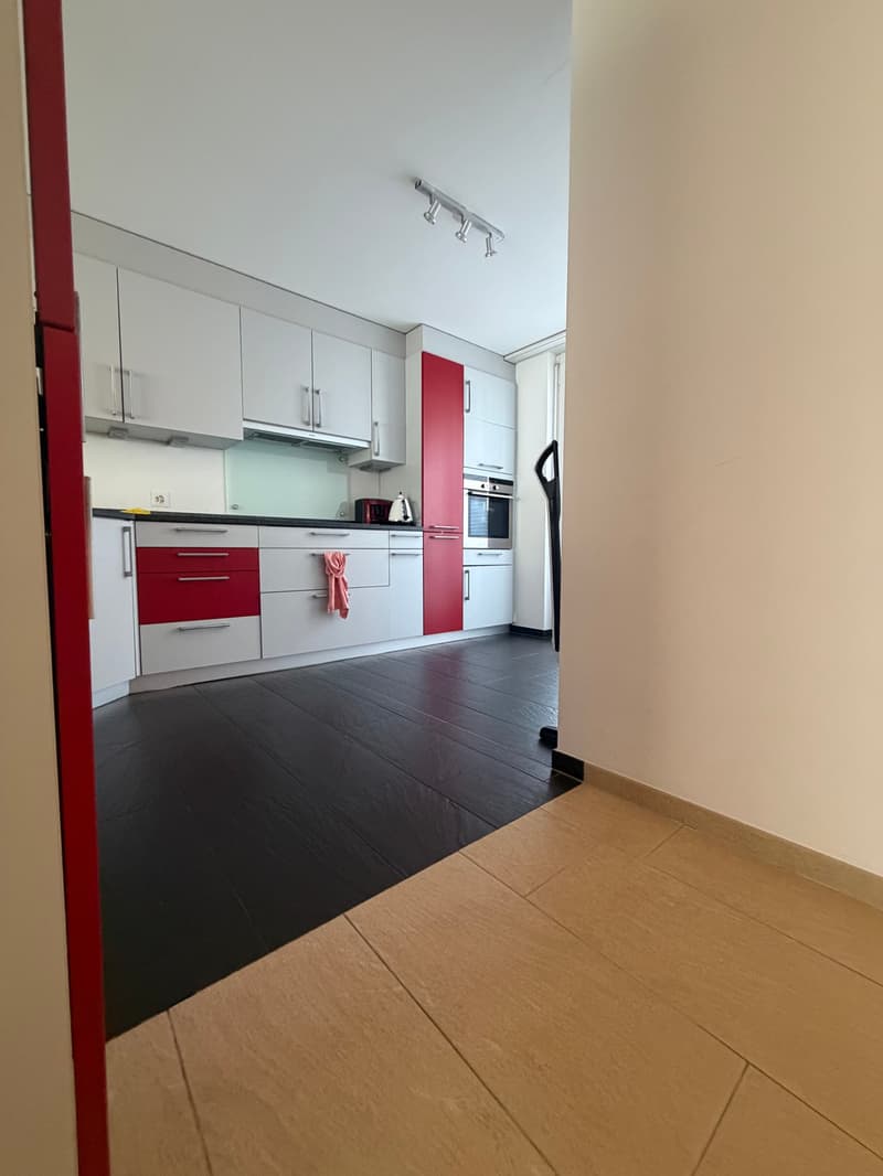 Modern kitchen with white cabinets, red accents, black tiled floor, wooden tiles on the side, kitchen appliances