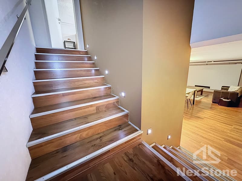 wooden staircase with white steps, beige wall, white railing, light fixtures on the wall