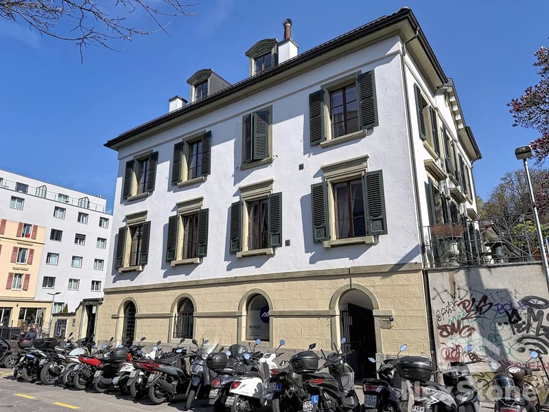 3 story building, white exterior, green shutters, arched windows, graffiti on wall, motorcycles parked in front