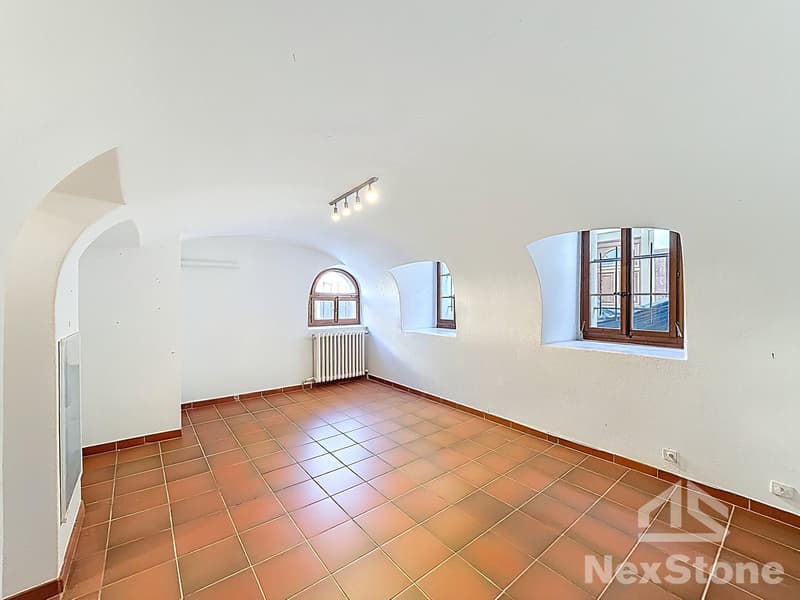 Empty room with arched ceiling, white walls, brown tiled floor, three arched windows, white radiator