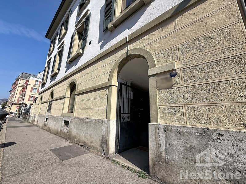 Stone building, arched entrance, multiple windows, black gate, street sign, sidewalk