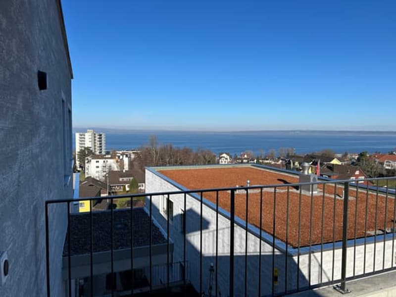 Building with a balcony, brown roof, metal railing, view of the ocean and town