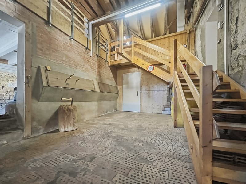 room with brick walls, wooden floor, wooden stairs, large stone on floor