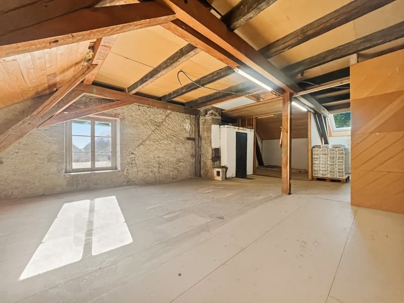 Exposed wooden beams, stone walls, small window, light mounted on the ceiling, open area with no furniture