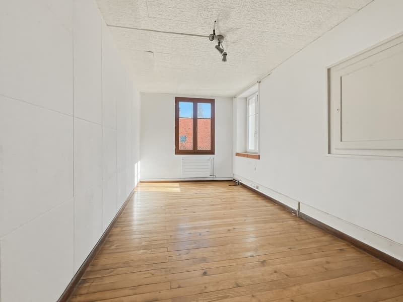 Empty room with wooden floors, white walls, and two windows.
