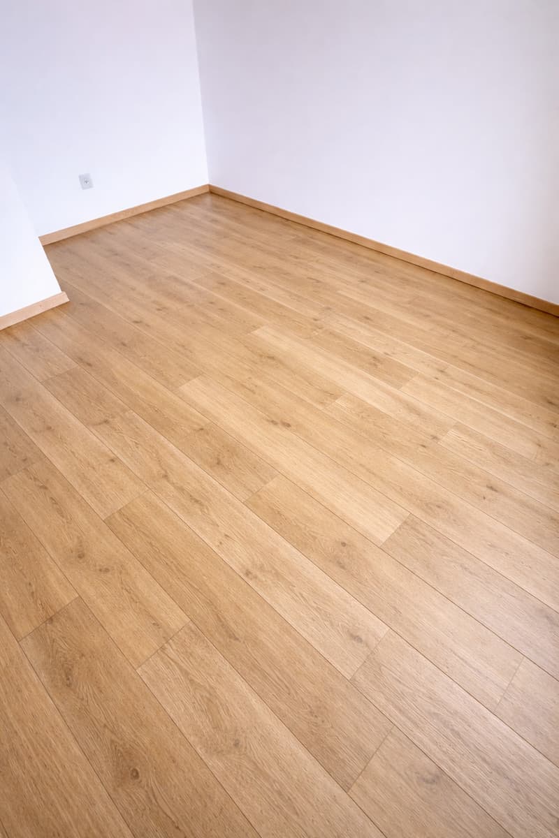 Empty room with hardwood floor, white walls, power outlet on wall.