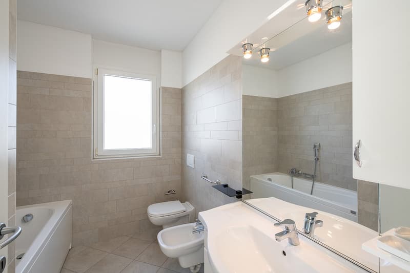 modern bathroom with bathtub, bidet, toilet, sink, mirror, and tiled walls