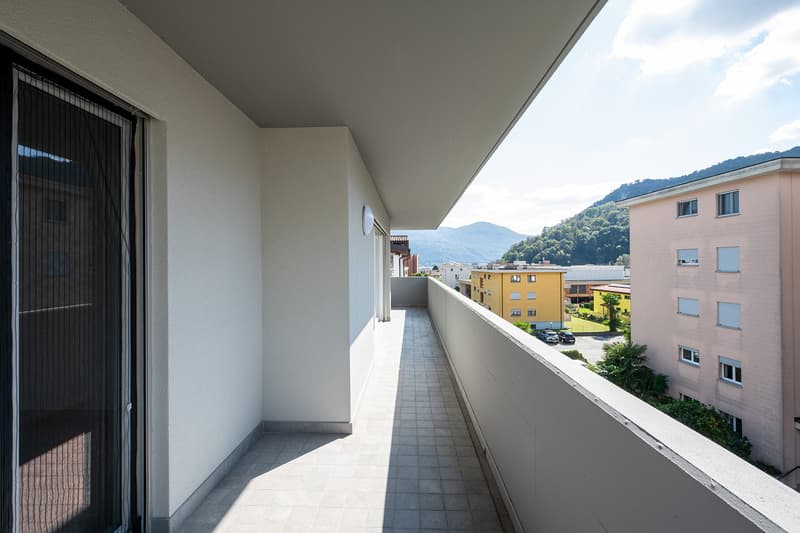 Balcony with tiled floor, white walls, railing, and a view of the mountains and buildings