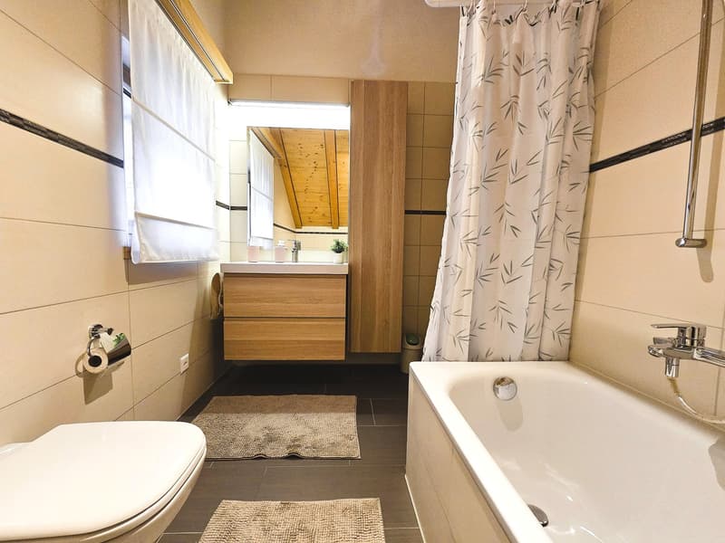 Bathroom with bathtub, shower, toilet, sink, wooden cabinet, and tiled floor.